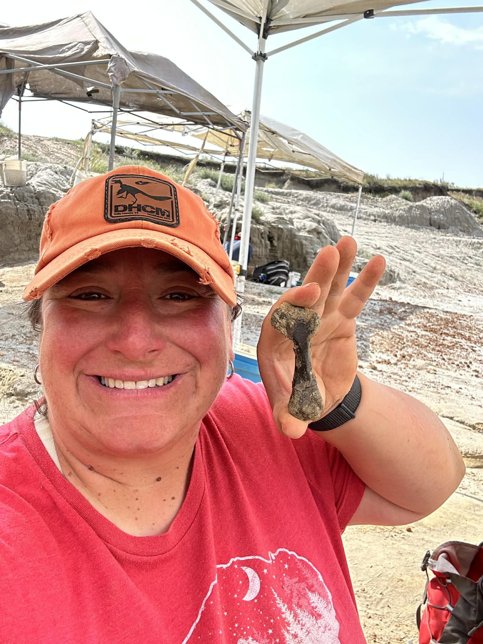 Jen Viele is pictured at a dig site holding a fossil and smiling. 